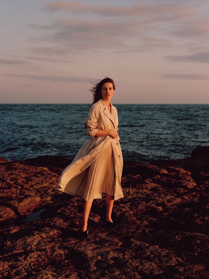 Woman in Trench Coat on Rocky Shore at Dusk