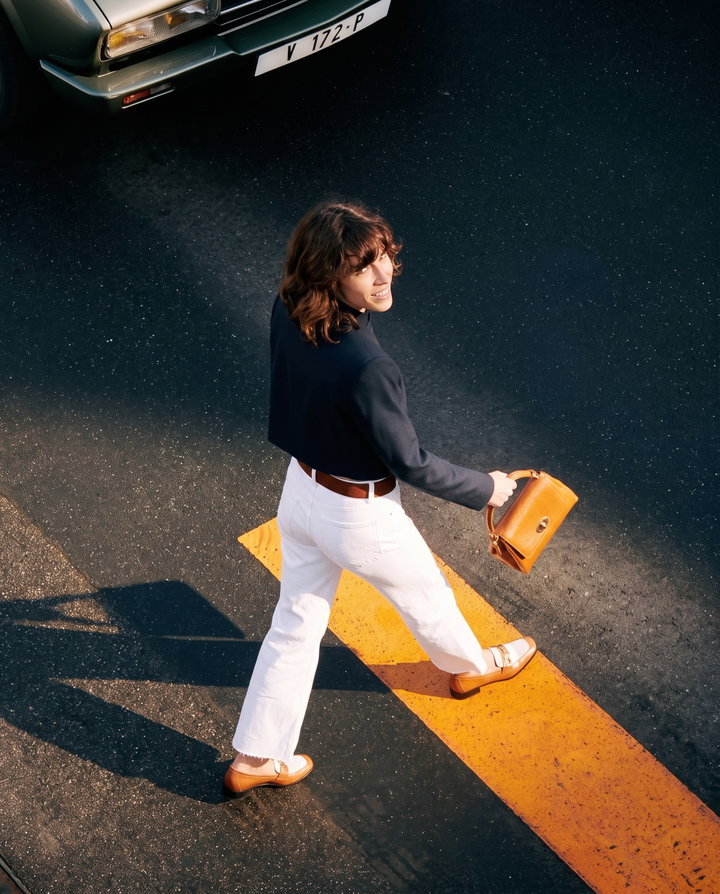 Woman Striding Across Street in Navy Jacket and White Jeans