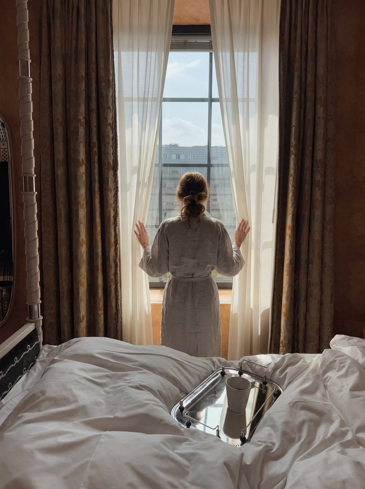 Woman in Grey Linen Robe Parting Sheer Curtains